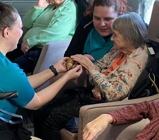 Kit, a resident at Haddington Care Home, smiling as she holds a snake during her 80th birthday celebration with ZooLabs, surrounded by staff, residents, and loved ones