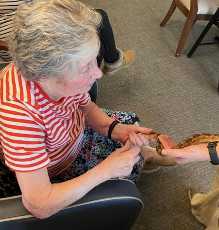 Kit, a resident at Haddington Care Home, smiling as she holds a snake during her 80th birthday celebration with ZooLabs, surrounded by staff, residents, and loved ones