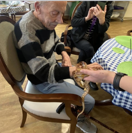 Kit, a resident at Haddington Care Home, smiling as she holds a snake during her 80th birthday celebration with ZooLabs, surrounded by staff, residents, and loved ones