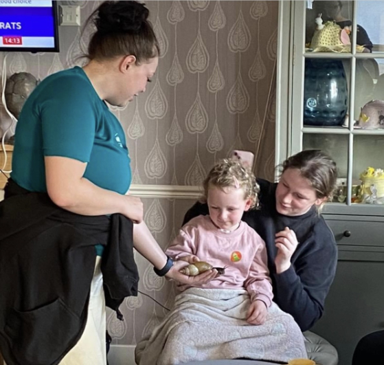 Kit, a resident at Haddington Care Home, smiling as she holds a snake during her 80th birthday celebration with ZooLabs, surrounded by staff, residents, and loved ones