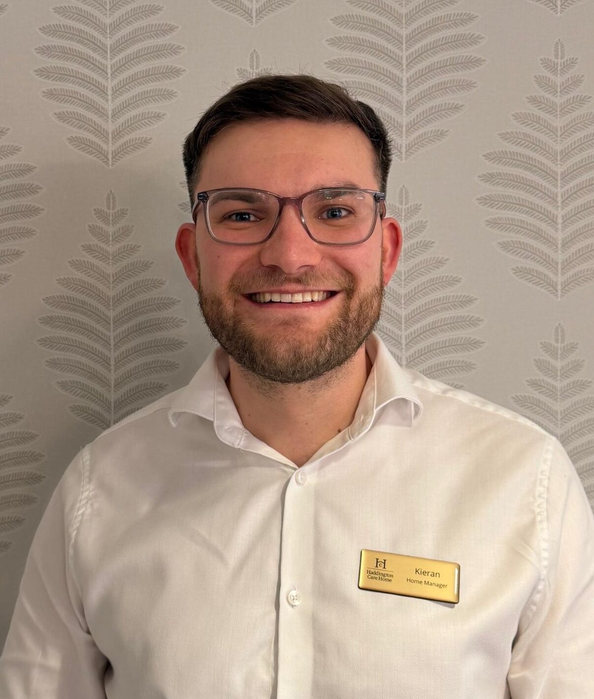 man in white shirt smiling in front of care home wallpaper