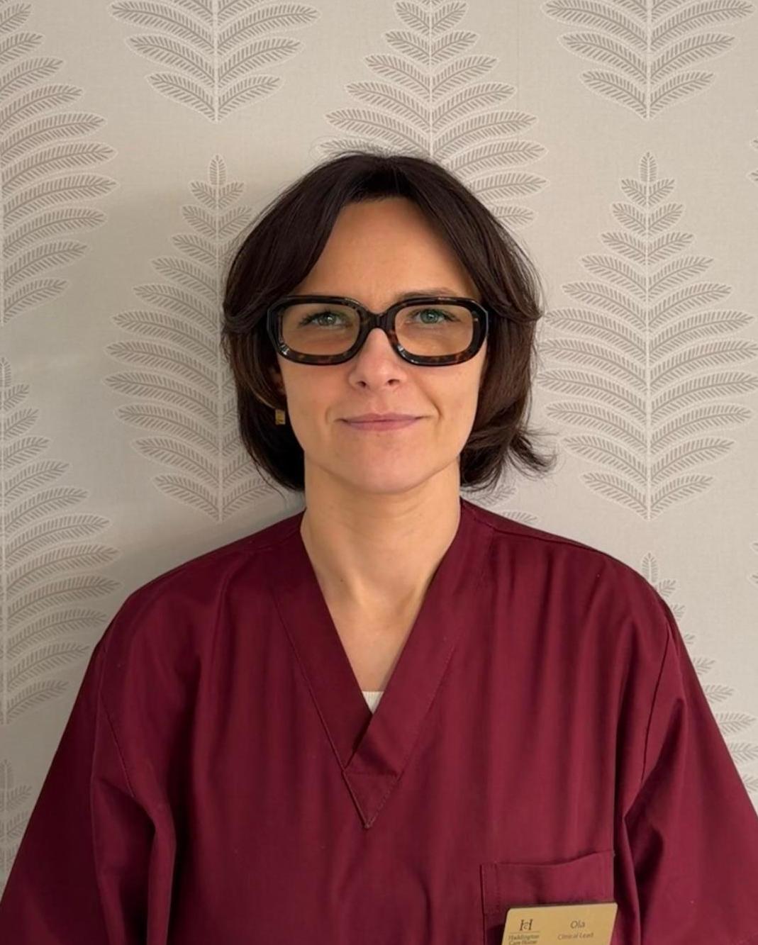 smiling woman with dark hair and glasses wearing a red nurses uniform