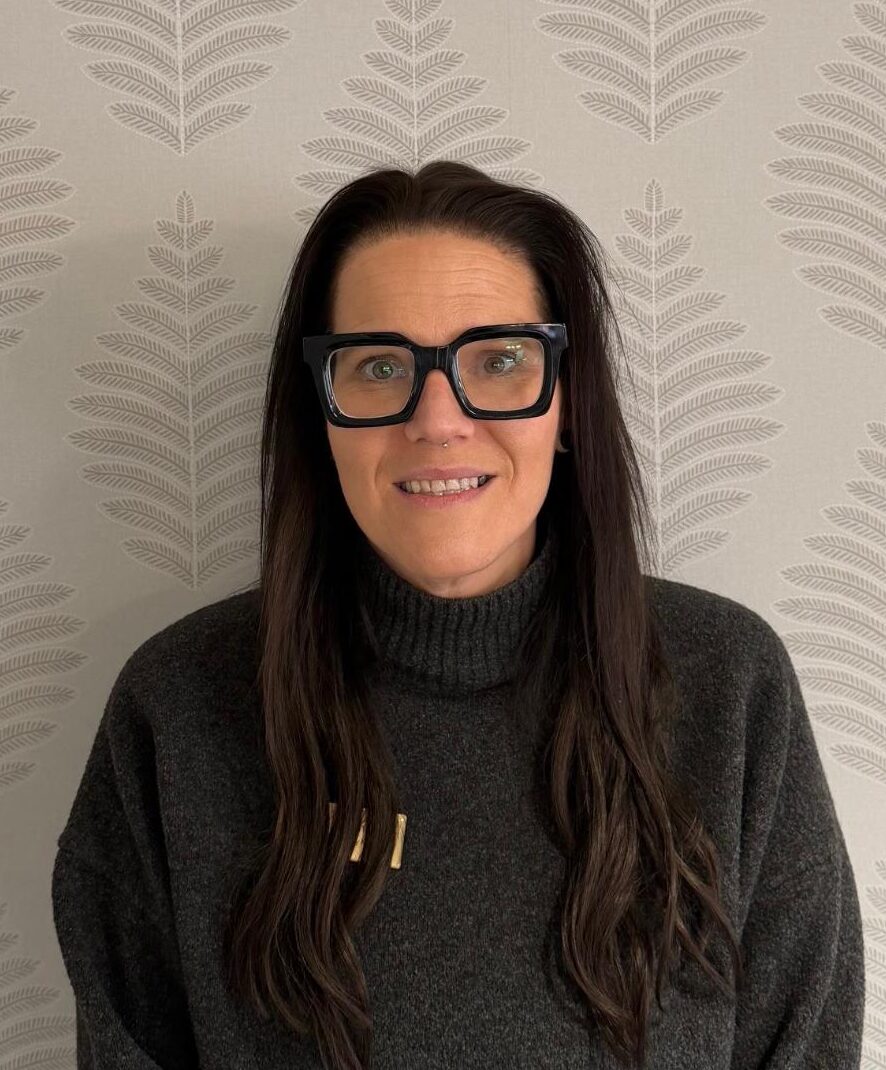 woman in grey knitted jumper and glasses smiling