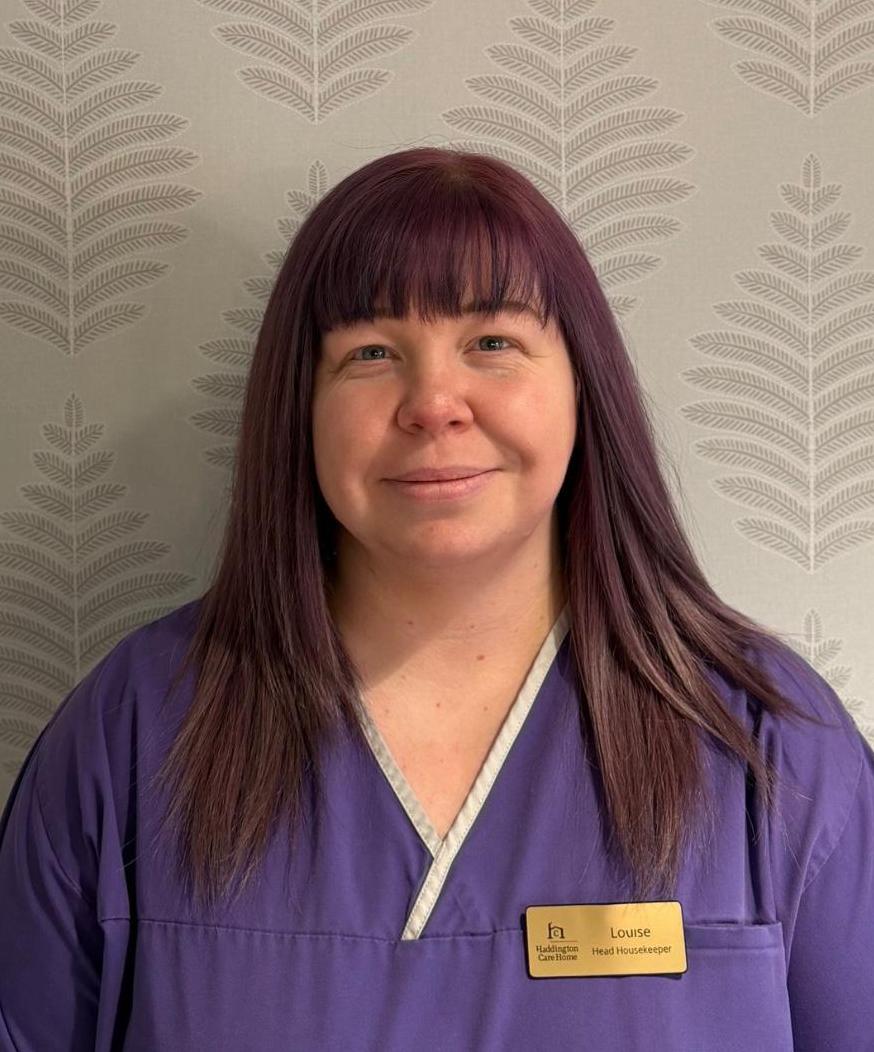 Woman with dark hair in purple nurses uniform smiles for headshot